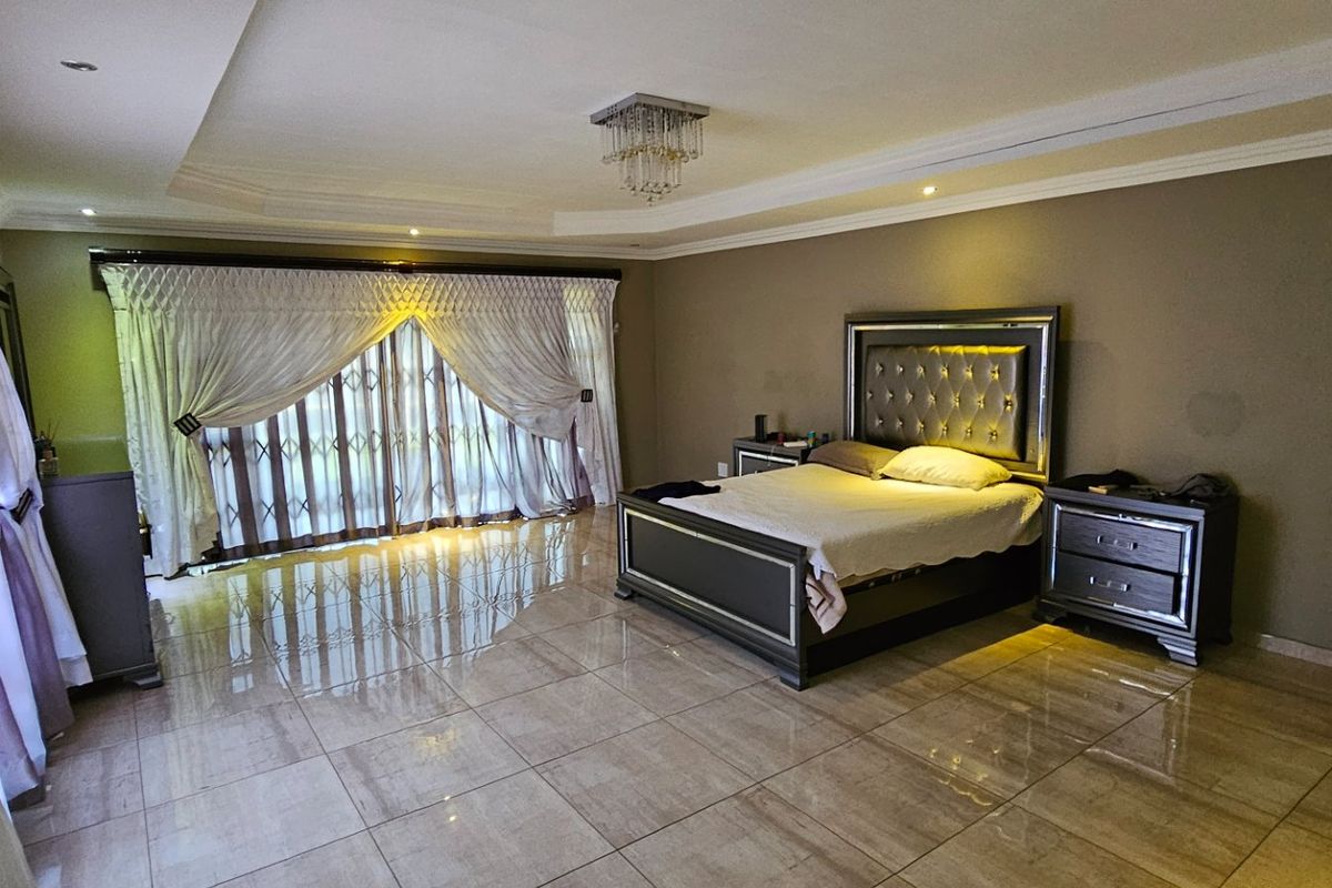 Spacious bedroom featuring polished tile flooring, recessed tray ceiling with decorative lighting, and large sliding glass doors leading to the exterior.