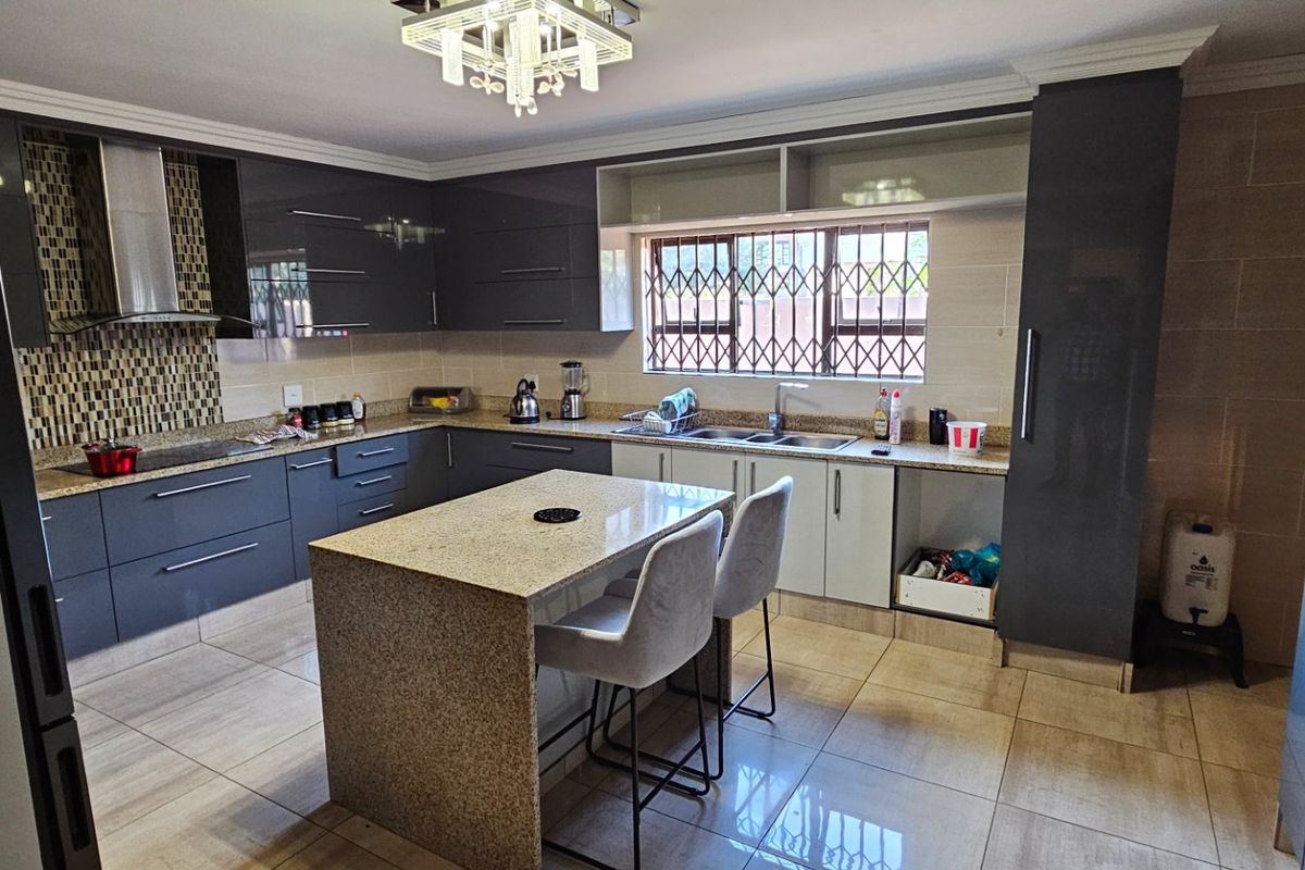 Modern kitchen featuring dark grey cabinetry, granite countertops, a central island, stainless steel extractor fan, and tiled flooring.