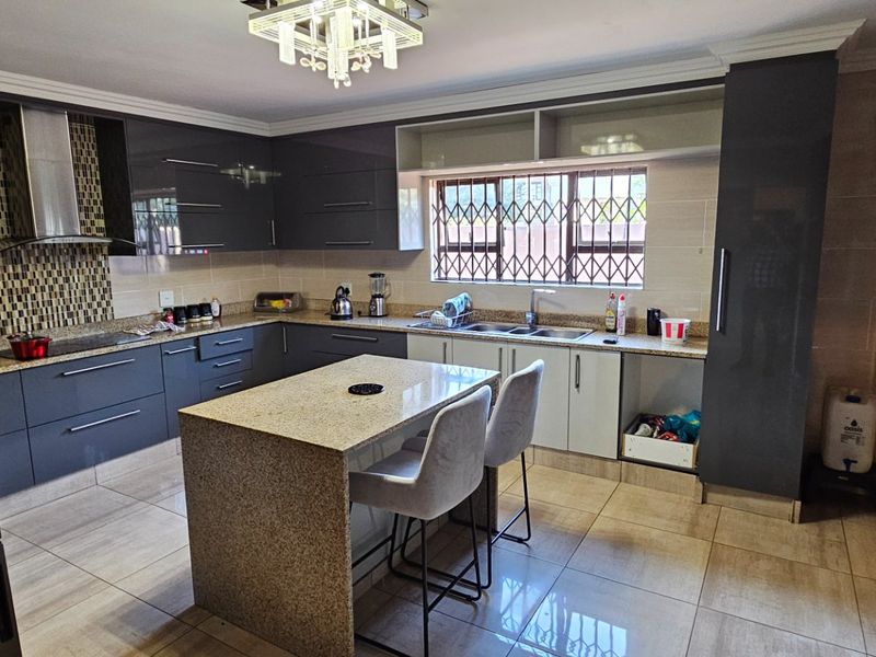 Modern kitchen featuring dark grey cabinetry, granite countertops, a central island, stainless steel extractor fan, and tiled flooring.