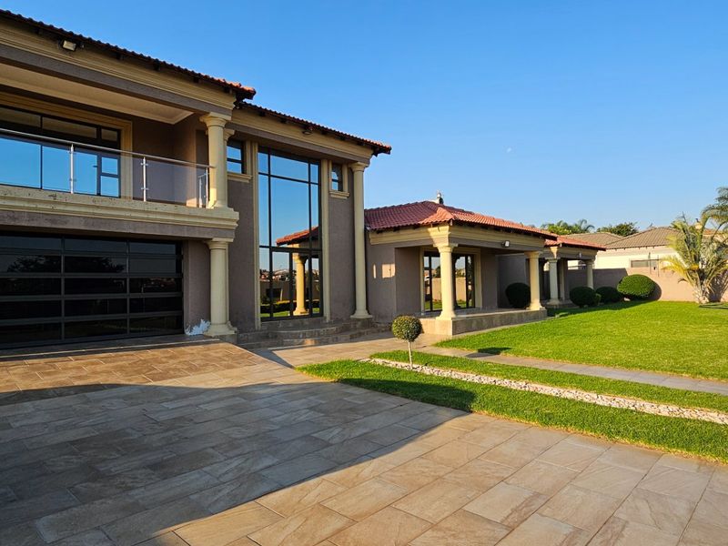 A spacious double-story residence featuring a paved driveway, large glass facade, balcony with glass balustrades, and a well-maintained garden.