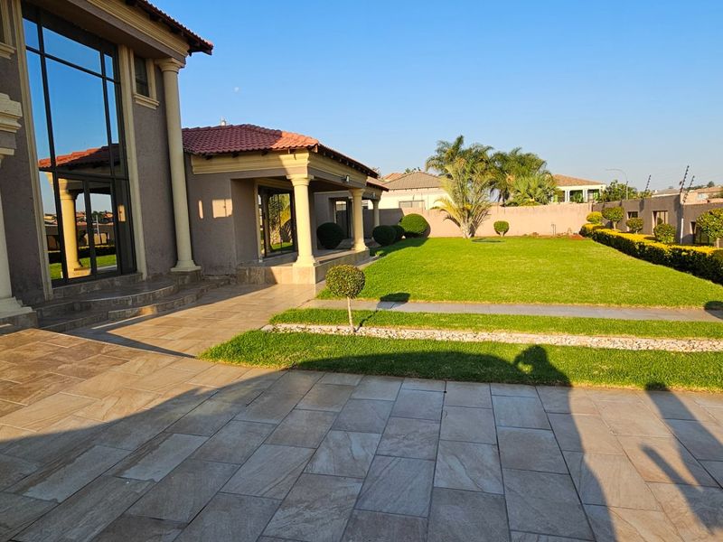 Spacious rear garden featuring a paved patio area, manicured lawn, and established landscaping, providing a private outdoor space for relaxation and entertainment.