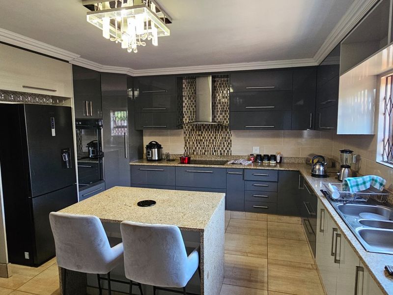 Modern kitchen featuring high-gloss cabinetry, granite countertops, a central island, built-in oven, extractor fan, and tiled flooring.