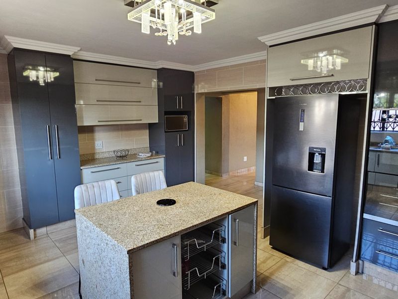 Modern kitchen featuring high-gloss cabinetry, granite countertops, a central island, and integrated appliances, finished with tiled flooring and contemporary lighting.