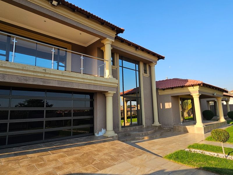 A modern double-story residence featuring a large glass garage door, a spacious upper balcony with glass balustrades, and a well-maintained garden.