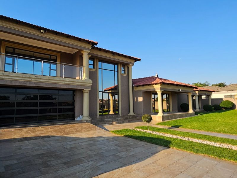 A spacious double-story residence featuring a modern glass garage door, expansive tiled driveway, and a well-maintained garden with covered patio areas.