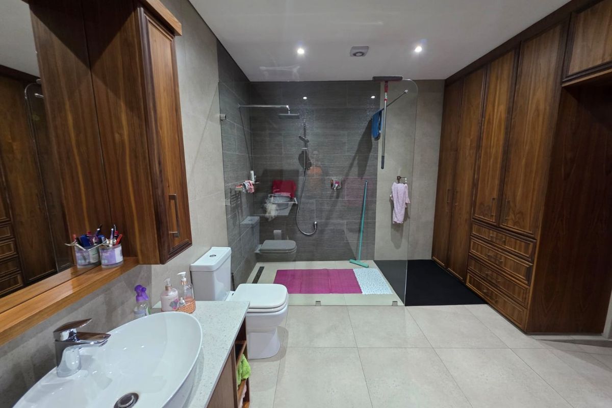 Modern bathroom featuring a walk-in glass shower, vessel sink vanity, built-in wooden cabinetry, and neutral floor-to-ceiling tiling.
