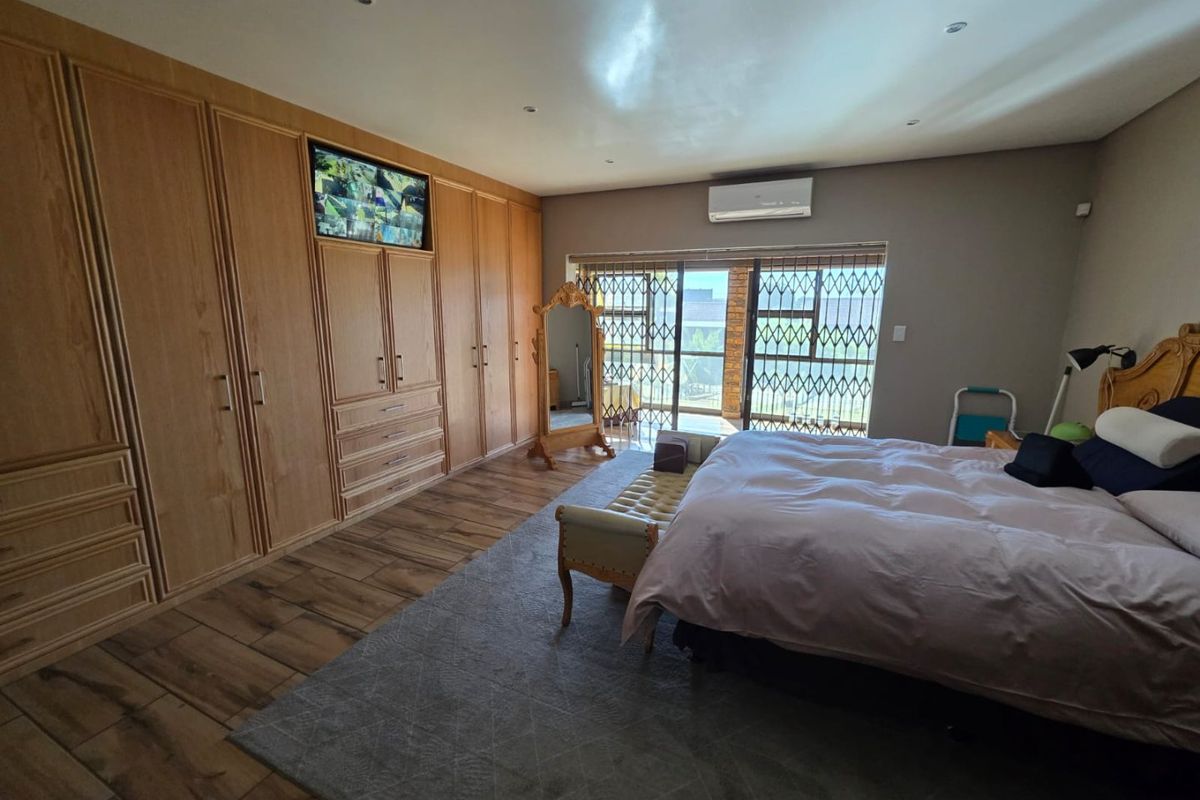 Spacious bedroom featuring extensive built-in wooden cabinetry, wood-look tiled flooring, recessed ceiling lighting, and a wall-mounted air conditioning unit.