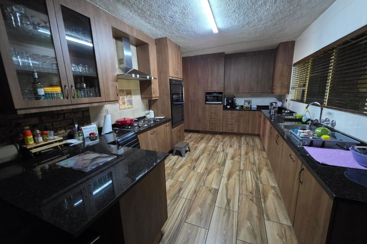 Spacious kitchen featuring dark wood cabinetry, granite countertops, built-in oven, extractor fan, and wood-look tiled flooring.