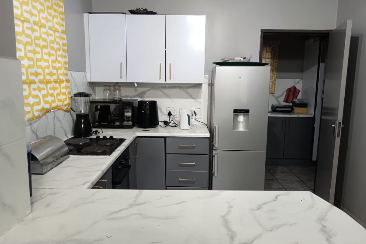 A functional kitchen featuring white upper cabinets, grey lower cabinetry, marble-effect countertops, and a built-in hob, with an adjacent scullery area.