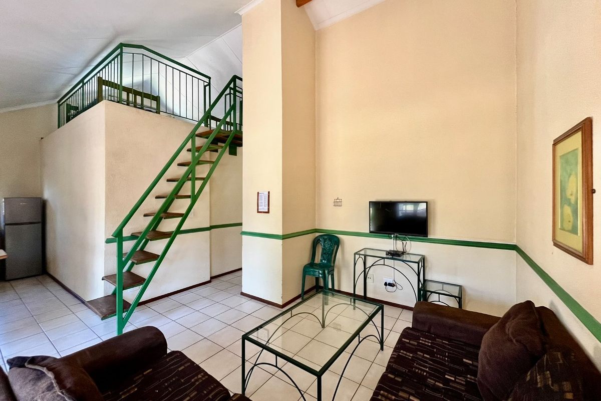 Living area featuring a mezzanine level with a metal staircase, tiled flooring, and high vaulted ceilings with an exposed wooden beam.