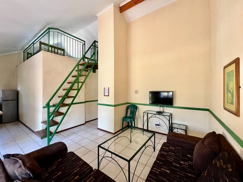 Living area featuring a mezzanine level with a metal staircase, tiled flooring, and high vaulted ceilings with an exposed wooden beam.