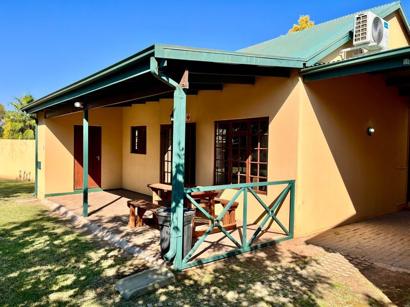 A covered patio area featuring paved flooring, timber window frames, and an external air conditioning unit, providing a functional outdoor space.