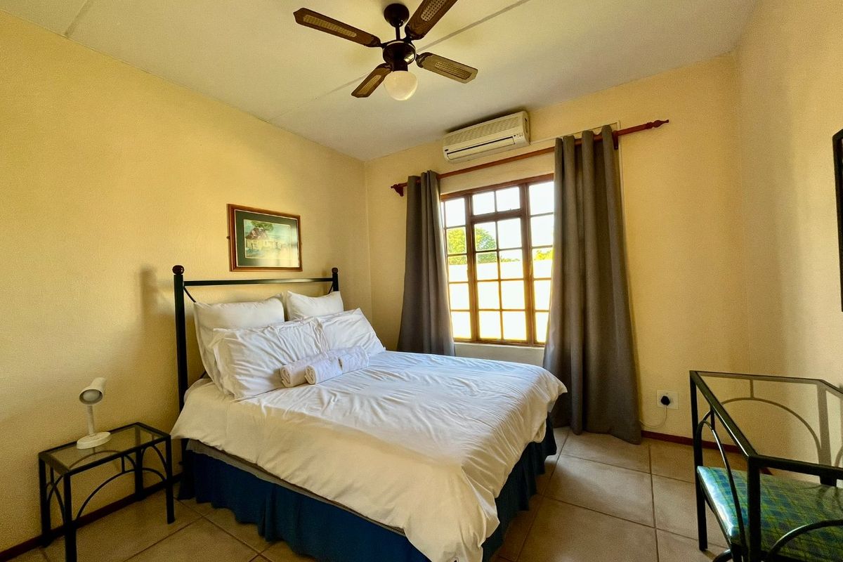 A functional bedroom featuring tiled flooring, a ceiling fan, and a wall-mounted split-system air conditioner for climate control.
