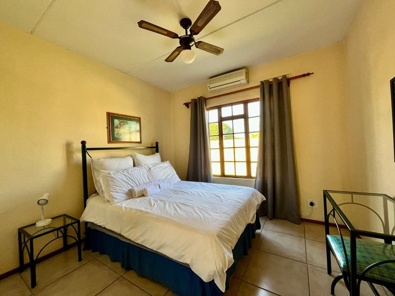 A functional bedroom featuring tiled flooring, a ceiling fan, and a wall-mounted split-system air conditioner for climate control.
