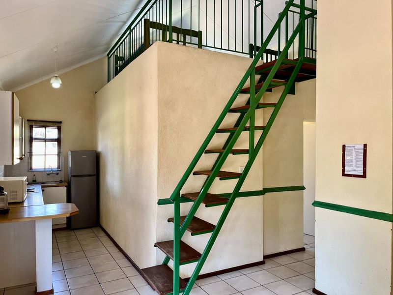 Open plan living area featuring a mezzanine level accessed by a metal staircase, tiled flooring, and a functional kitchen space.