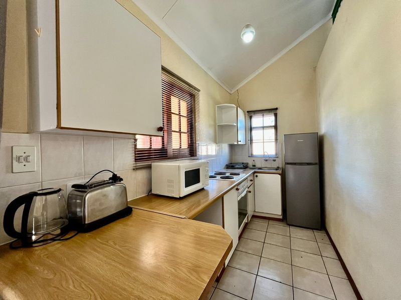 A compact kitchen featuring laminate countertops, built-in cabinetry, a built-in oven with hob, and tiled flooring, offering a functional layout for daily use.