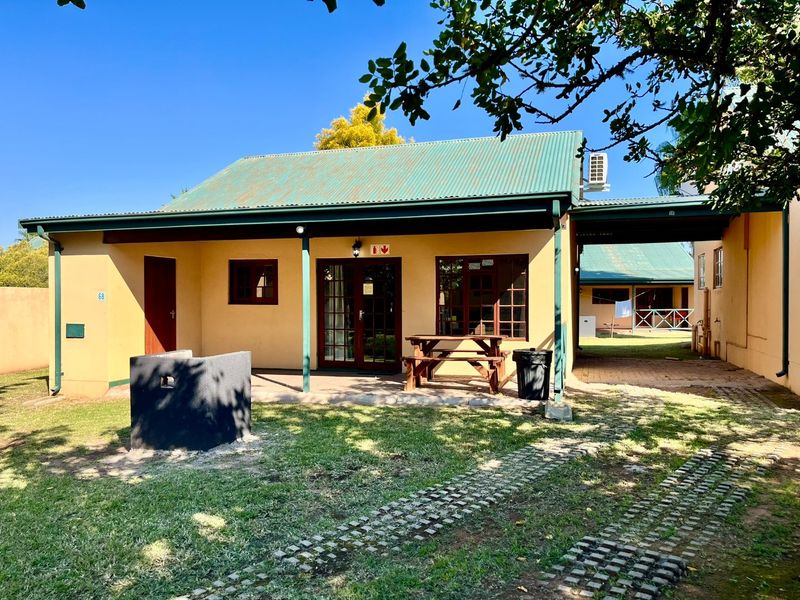 Rear view of the property featuring a covered patio, built-in brick braai, paved driveway, and a corrugated metal roof.