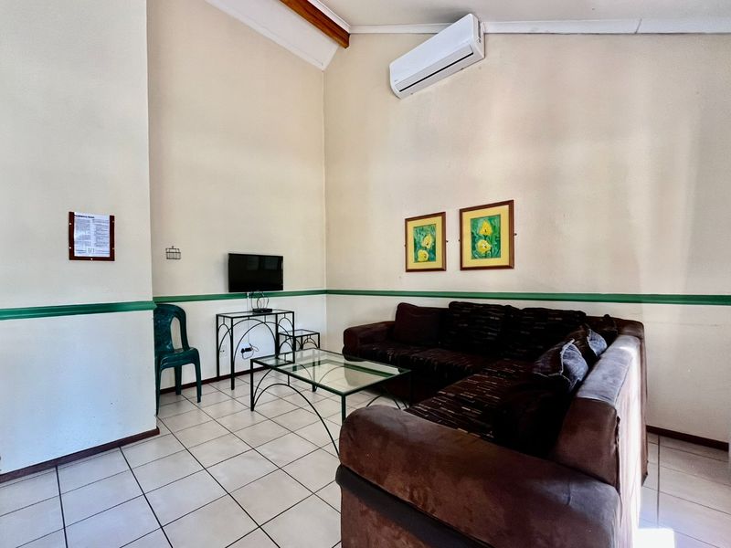 A living room featuring ceramic floor tiles, a wall-mounted split-system air conditioner, and decorative chair rail molding.