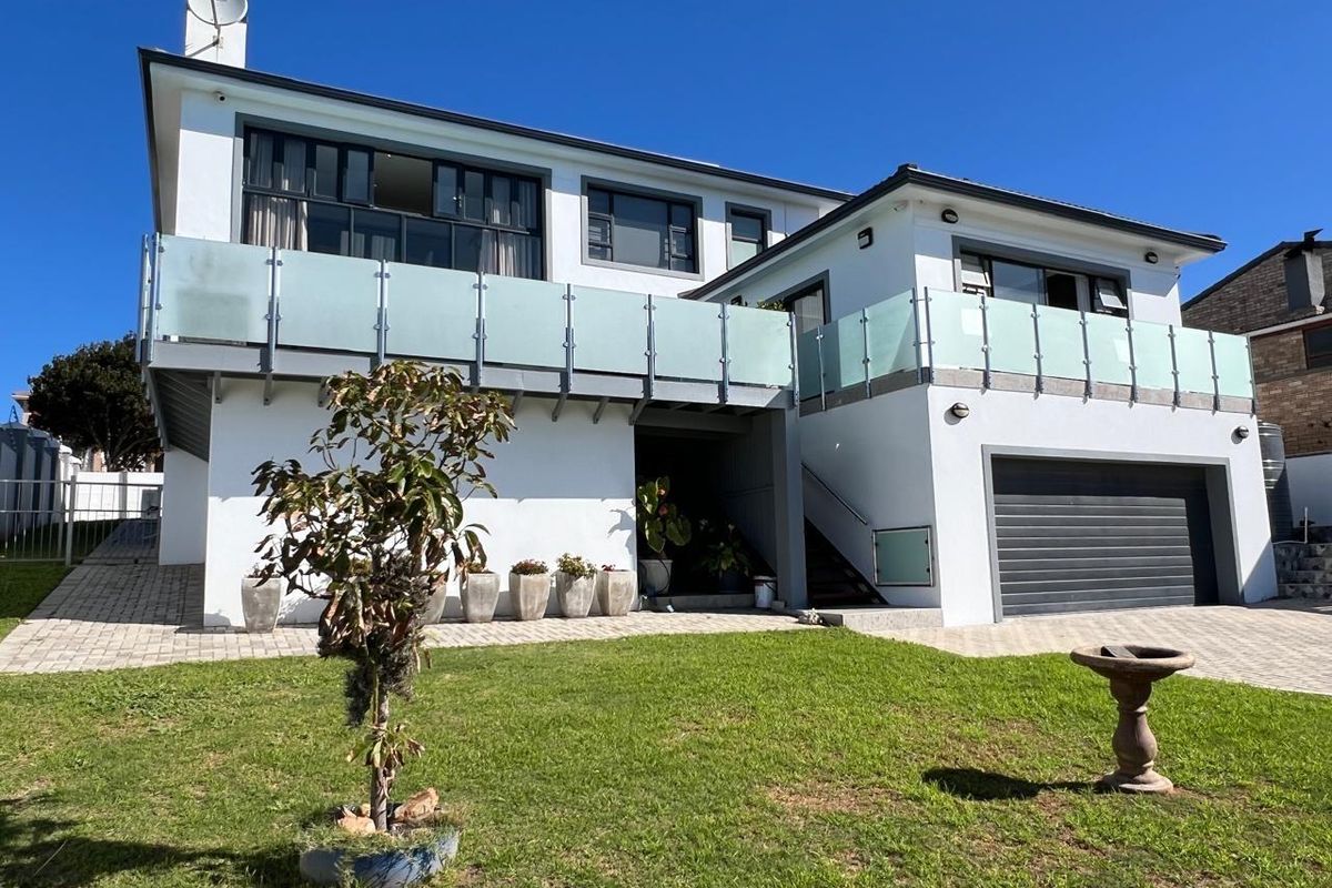Rear view of a modern two-story house featuring a large glass-balustrade balcony, paved driveway, and integrated double garage.
