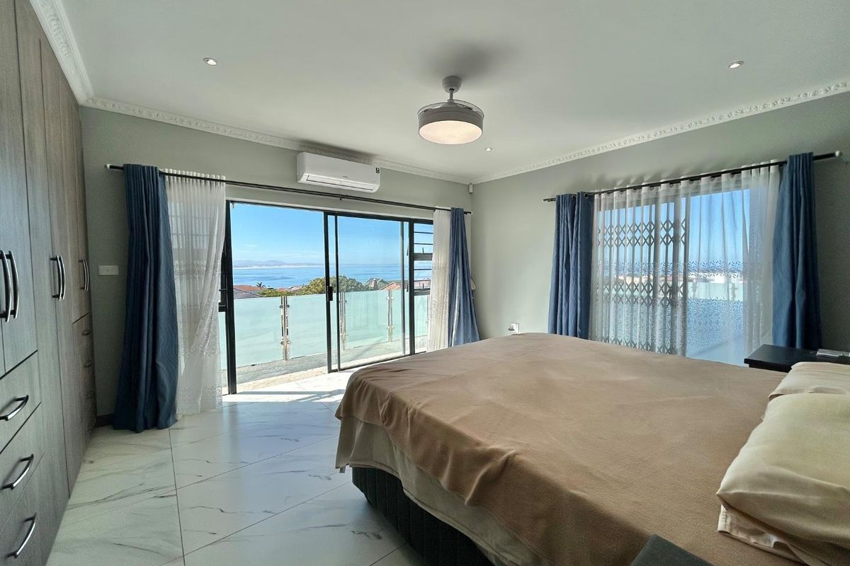 Spacious bedroom featuring marble-look flooring, built-in cupboards, air conditioning, and sliding doors opening to a balcony with expansive ocean views.