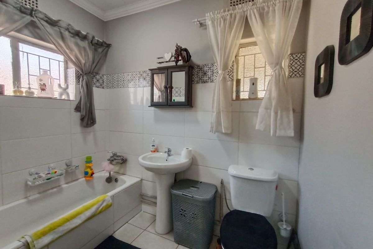A functional bathroom featuring a white pedestal basin, a standard bathtub with shower mixer, and a toilet, finished with decorative wall tiling.