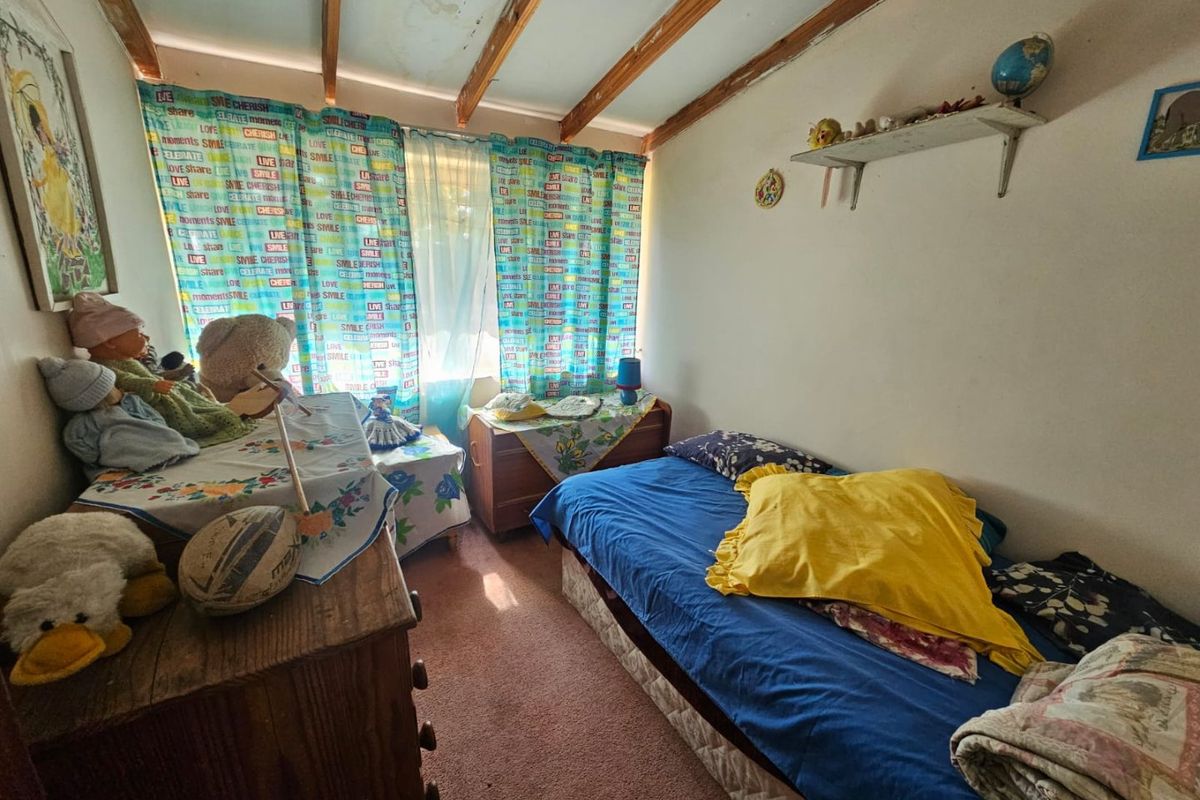 A bedroom featuring exposed timber ceiling beams, showing signs of water damage and wear, requiring maintenance and cosmetic updates.