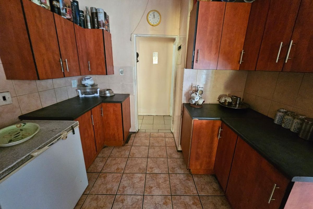 A dated galley-style kitchen featuring wood-look laminate cabinetry, dark countertops, and ceramic tile flooring, offering potential for a modern renovation.