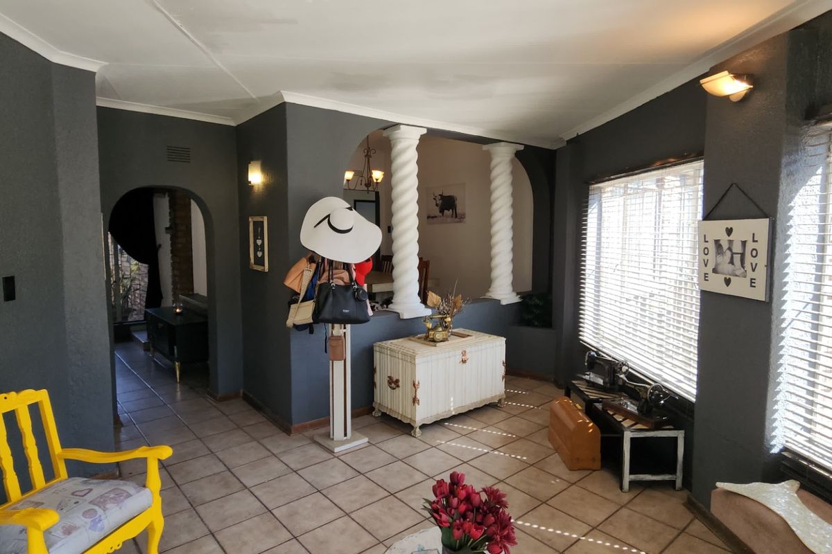 A living area featuring decorative columns, tiled flooring, and large windows with fitted blinds, creating a distinct transition between living and dining spaces.