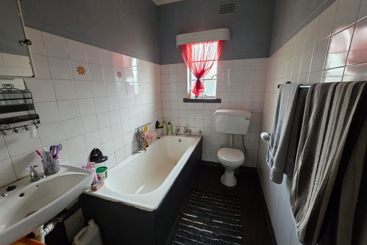 A compact bathroom featuring a standard bathtub, pedestal basin, and toilet, with half-tiled walls and a functional layout.
