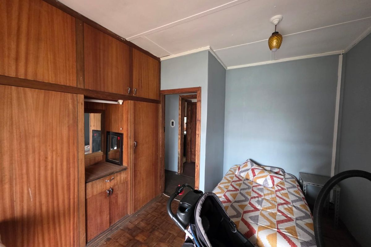 A bedroom featuring extensive built-in wooden cabinetry, parquet flooring, and a neutral wall finish, offering a functional space with potential for modernization.