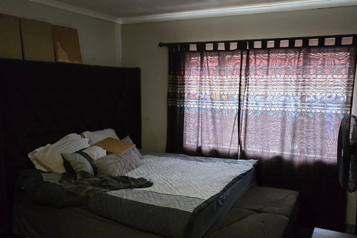 A bedroom featuring a large headboard, window with curtain rod, and neutral wall finishes.
