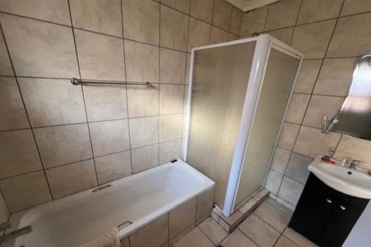 A functional bathroom featuring a built-in bathtub, a separate shower enclosure, and a wall-mounted vanity basin with tiled walls and flooring.