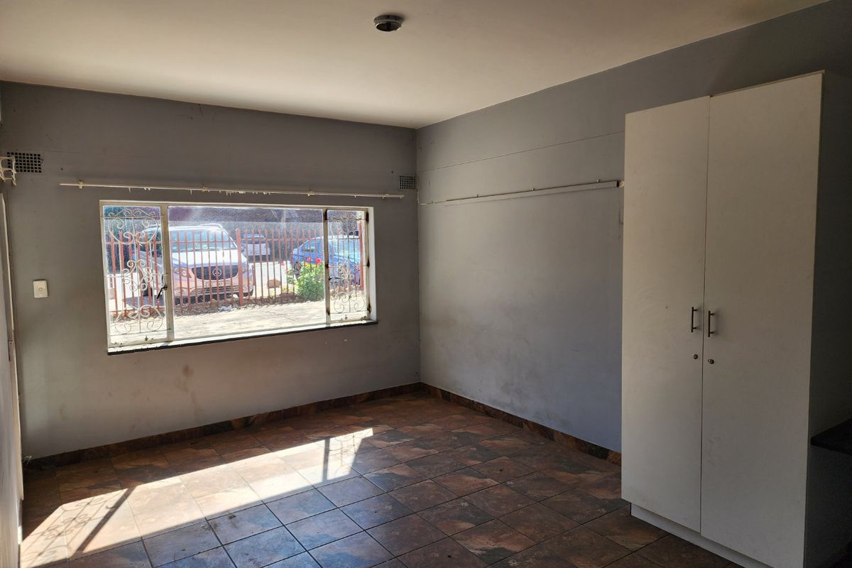 A bedroom featuring tiled flooring, a built-in wardrobe, and a window with security bars overlooking the exterior.