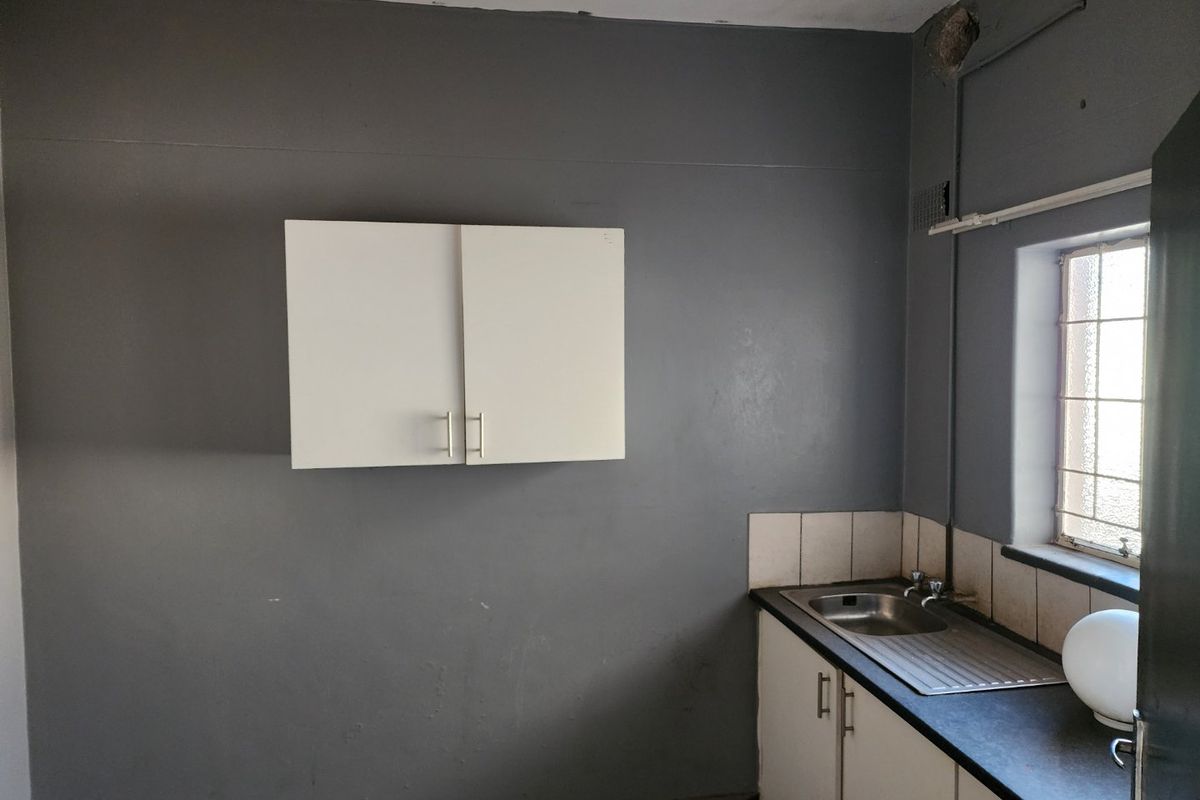 A compact kitchen area featuring basic cabinetry, a stainless steel sink, and a window, requiring cosmetic updates to improve functionality and aesthetic appeal.