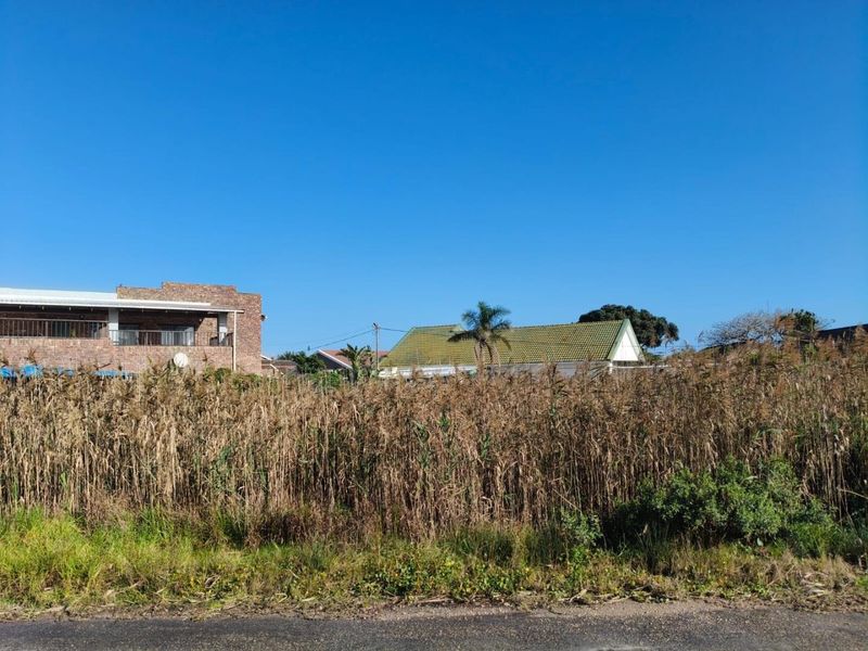 A view of a vacant residential plot featuring overgrown vegetation, situated in a developed neighborhood with surrounding residential properties.
