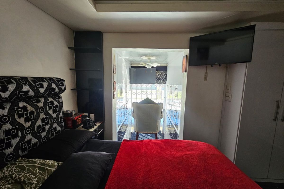 A bedroom featuring built-in shelving and a wall-mounted television, with direct access to an enclosed patio area through a security gate.