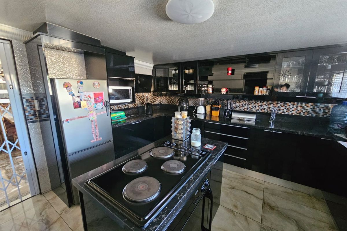 Modern kitchen featuring black cabinetry, granite countertops, a central island with a built-in electric hob, and tiled flooring.
