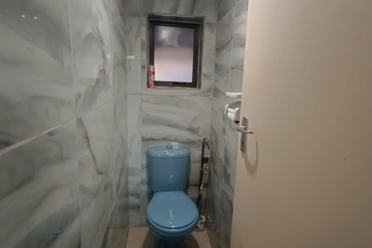 A compact guest bathroom featuring floor-to-ceiling marble-effect wall tiles, a small window, and a blue toilet suite.