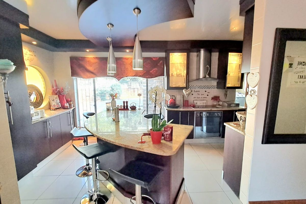 Modern kitchen featuring a large granite island, custom bulkhead ceiling with pendant lighting, built-in oven, extractor fan, and ample cabinetry.