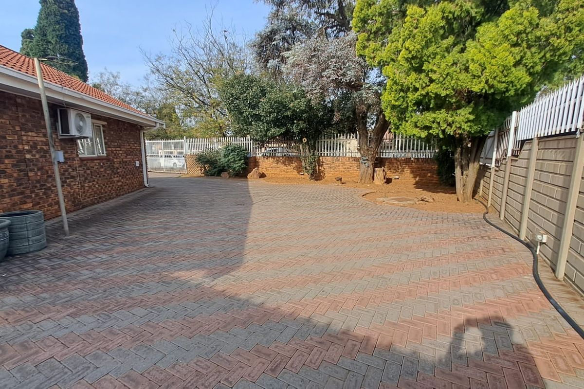 A spacious rear exterior area featuring durable brick paving, a face brick building facade, and secure perimeter walling with spiked fencing.