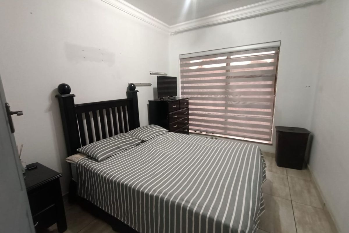 A standard bedroom featuring tiled flooring, crown molding, and a large window fitted with modern zebra blinds.