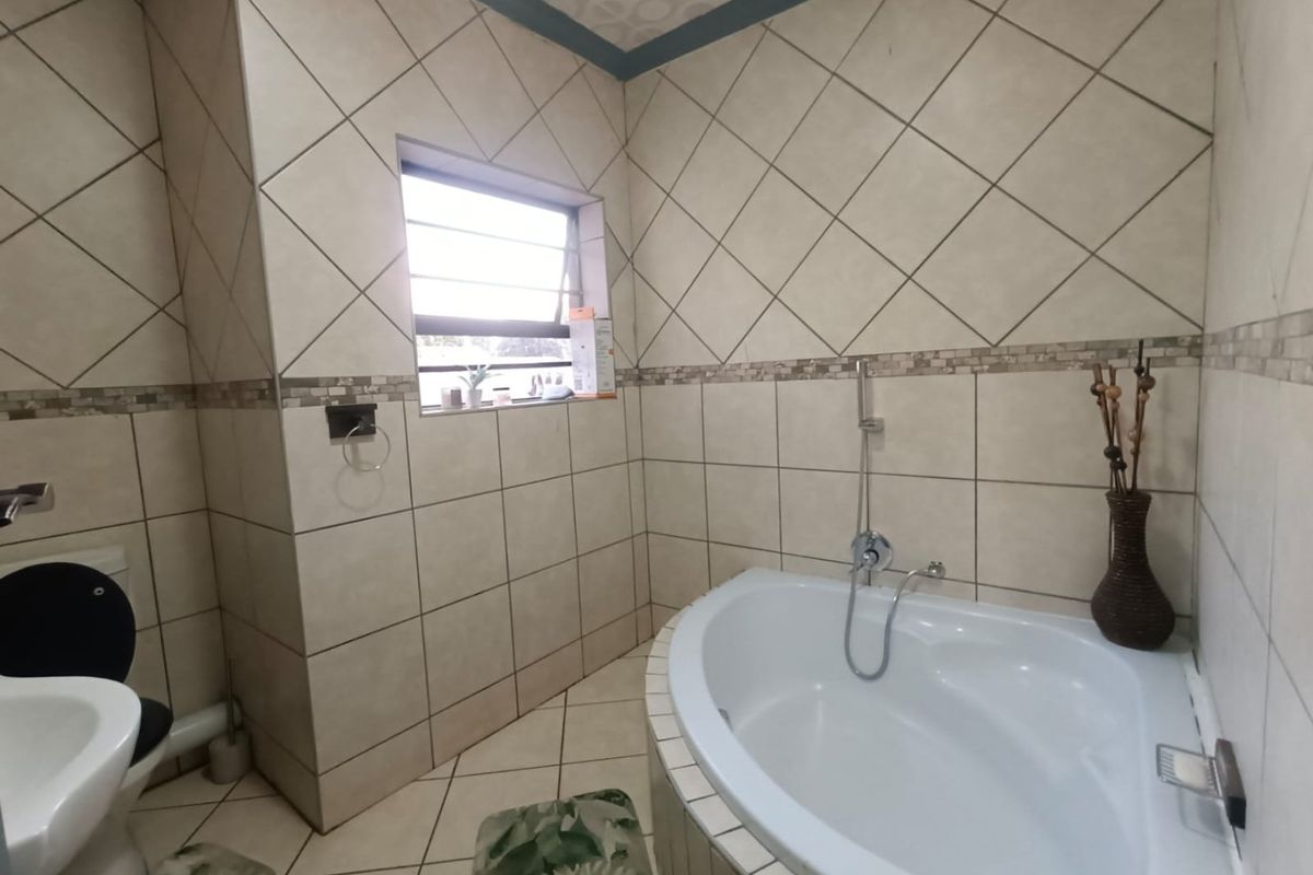 A functional bathroom featuring a corner bathtub, tiled walls with decorative border, and a standard toilet.