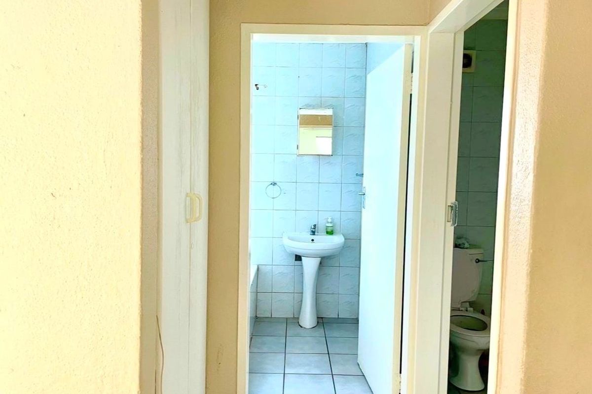 A view into a dated bathroom featuring a pedestal basin, tiled walls, and floor, requiring cosmetic updates to modernize the space.