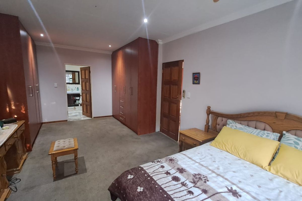 Spacious bedroom featuring extensive built-in wooden cabinetry, recessed downlighting, and direct access to an en-suite bathroom.