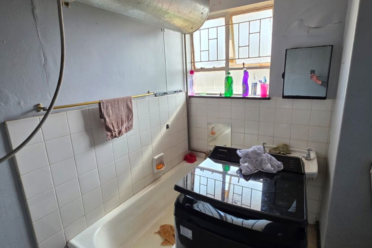 A dated bathroom featuring a built-in bathtub, wall-mounted geyser, and tiled flooring, requiring significant renovation and cosmetic updates.