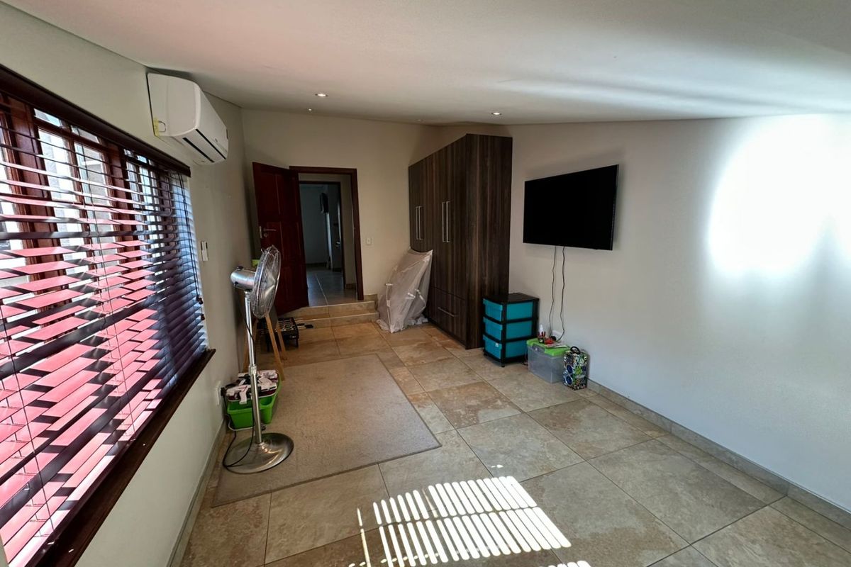 A living room featuring large format floor tiles, a wall-mounted air conditioning unit, and built-in cabinetry, providing a functional and versatile living space.