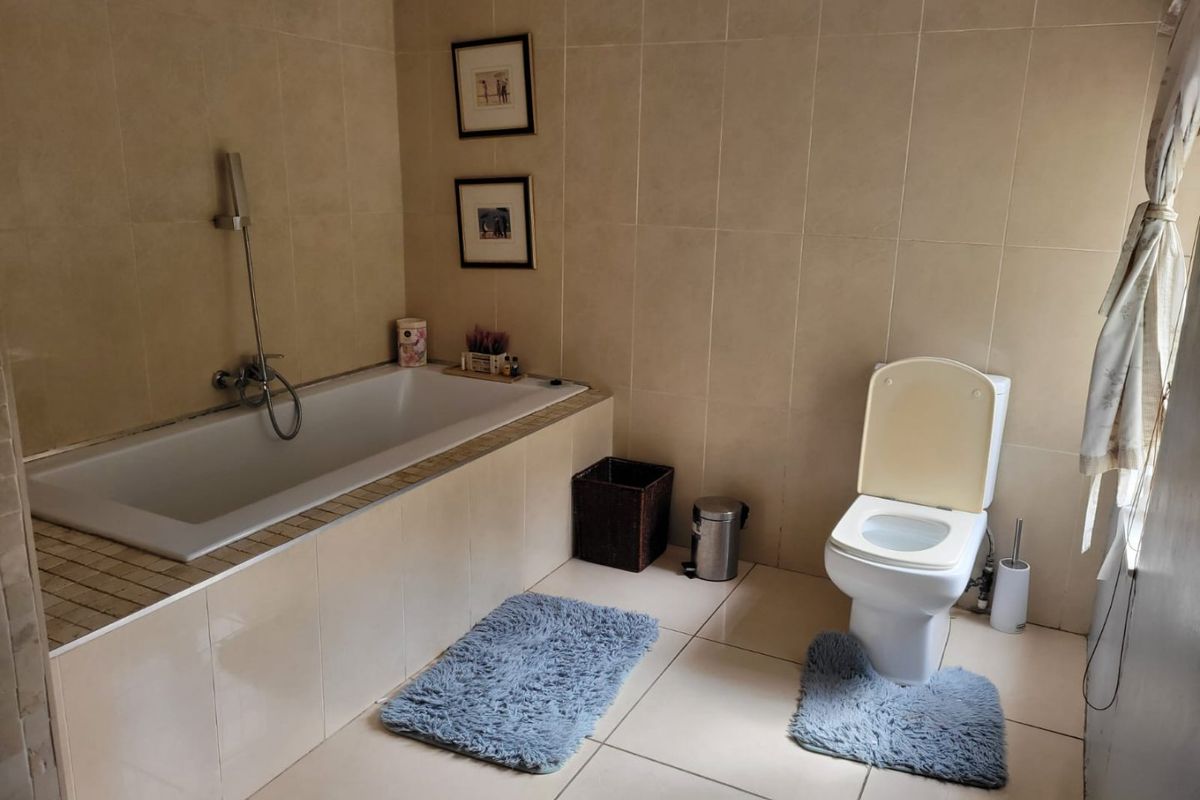 A functional bathroom featuring a built-in bathtub with shower mixer and a standard toilet, finished with neutral wall and floor tiling.