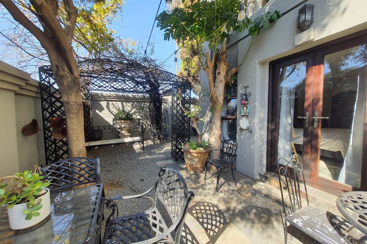 A private rear courtyard featuring a metal pergola, gravel flooring, and direct access to the interior through double glass doors.