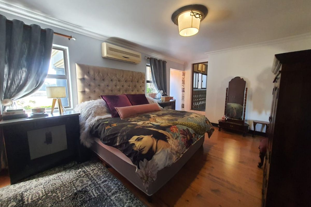 A spacious bedroom featuring polished wooden flooring, a wall-mounted air conditioning unit, and large windows allowing for natural light.