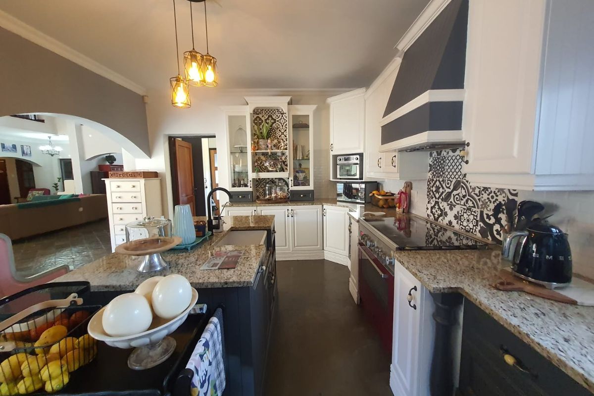 A well-appointed kitchen featuring granite countertops, a central island, built-in oven, extractor fan, and decorative patterned tile backsplash.